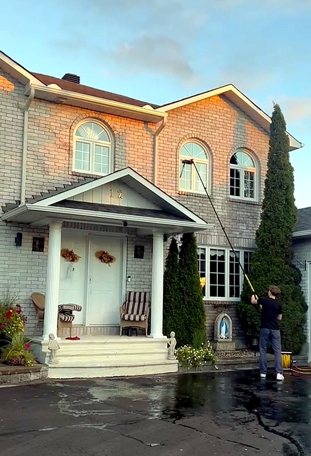 Window Brothers cleaning the upper arched windows of a two-storey brick home with a pure-water pole at golden hour