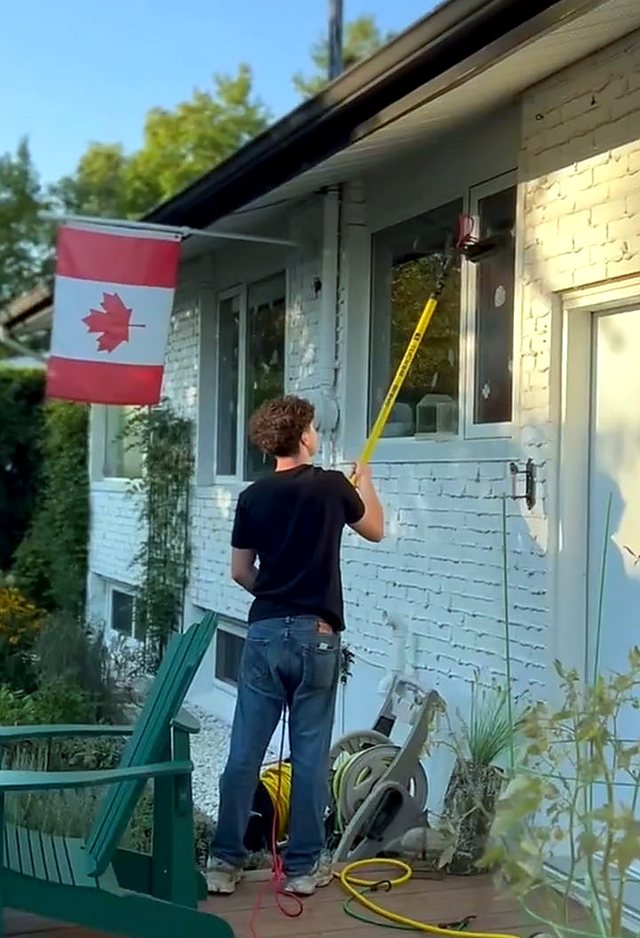 Cleaning the windows of a white-brick bungalow with a Canadian flag flying